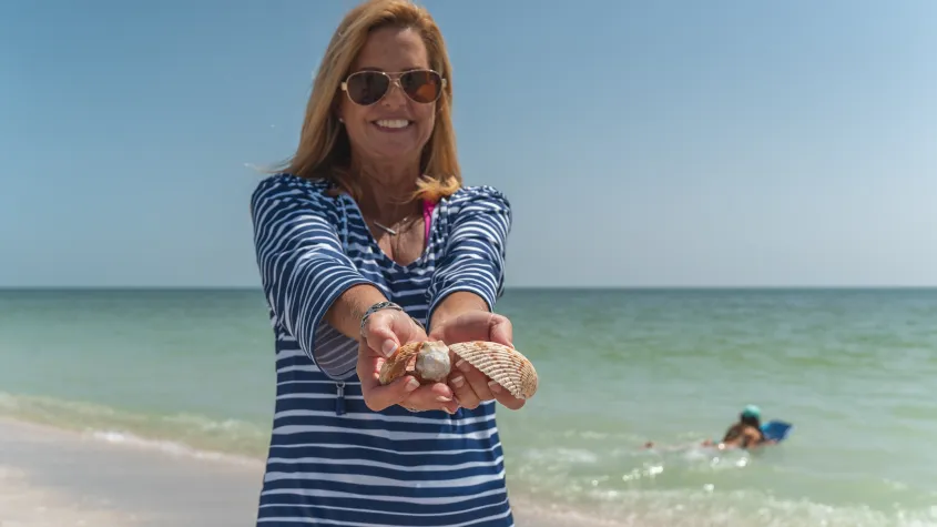 Smiling woman holding shells with beach background