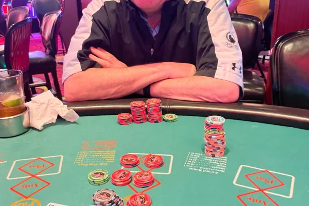 Man in Detroit cap smiles at poker table with chips and cards in casino
