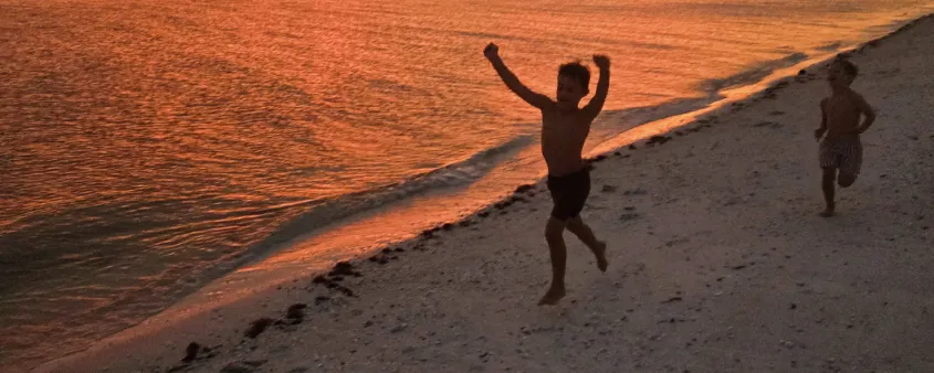 A kid runs happily on the beach at sunset